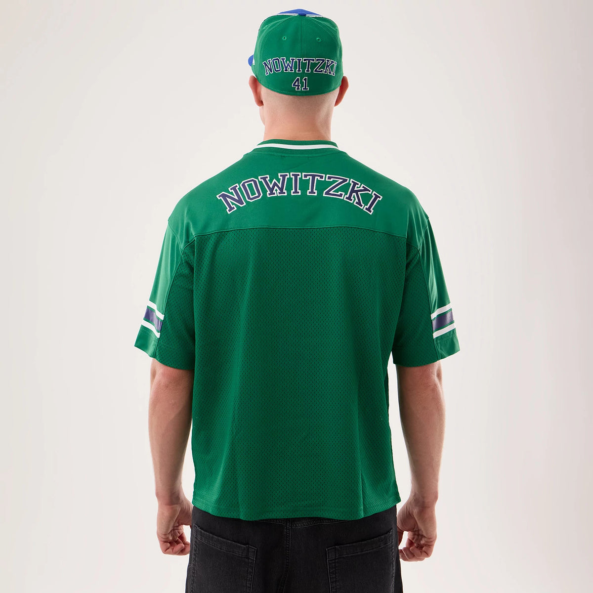 New Era Dallas Mavericks NBA Hardwood Classic Mesh Oversized Green T-Shirt, back view on a model with a matching cap, showing Nowitzki lettering prominently across the upper back, along with horizontal stripes on the short sleeves and a relaxed fit.