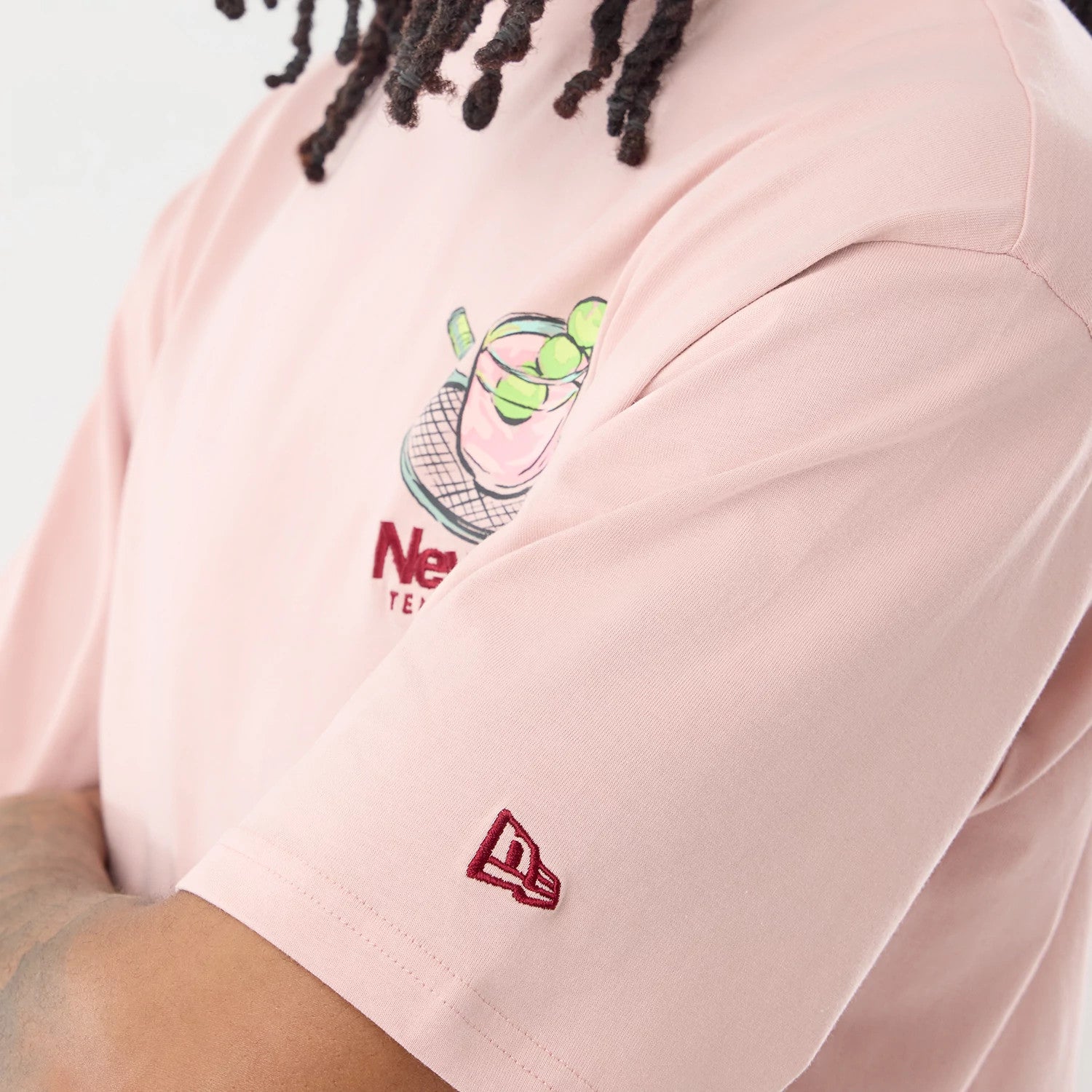 The model is wearing this New Era Tennis Graphic Oversized T-Shirt in pastel pink. 7