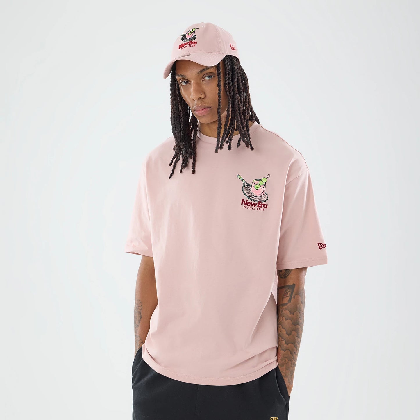 The model is wearing this New Era Tennis Graphic Oversized T-Shirt in pastel pink. 1