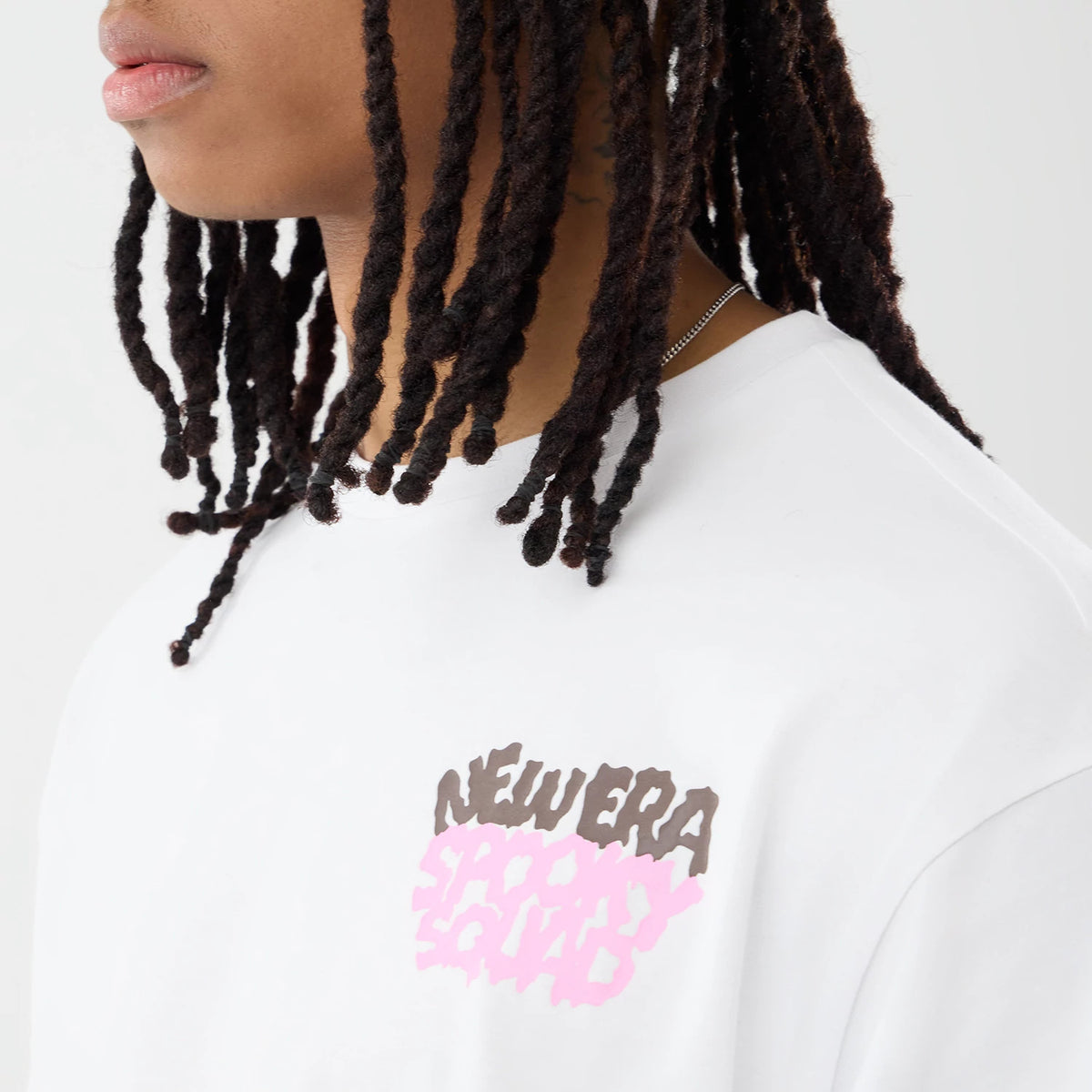 New Era Spooky Graphic Oversized White T-Shirt, on-model view focusing on the small front graphic with the words NEW ERA SPOOKY SQUAD in brown and pink printed on the left chest, highlighting the casual fit and simple neckline.