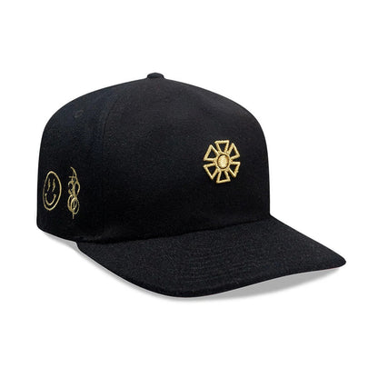 New Era X Omerta Balvin Black 19TWENTY Adjustable Cap, front view showing a gold embroidered geometric logo on the front panel, with additional gold smiley face and abstract designs on the side, and a curved black visor.