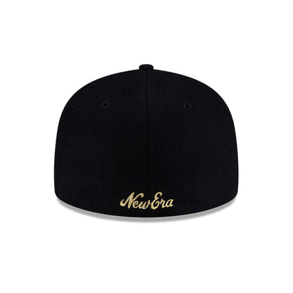 New Era X Omerta Balvin Black 59FIFTY Fitted Cap, side view showing gold embroidered smiley face and abstract design on the structured black crown, with a curved black visor and New Era flag logo on the left side.