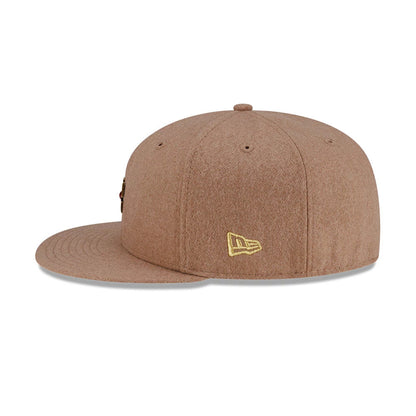 New Era X Omerta Balvin Beige 59FIFTY Fitted Cap, front view showing a central ornate cross emblem embroidered on the beige front panel, matching the beige structured crown and flat visor with eyelets and top button.