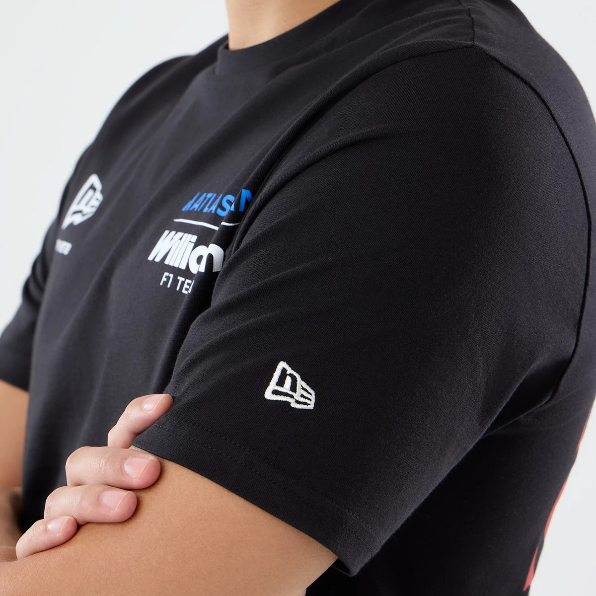 New Era Williams Carlos Sainz Spain Race Special Black T-Shirt, side view on-model showing the embroidered New Era flag logo on the sleeve, printed Williams F1 team logo on the chest, and contrasting blue and white sponsor lettering.