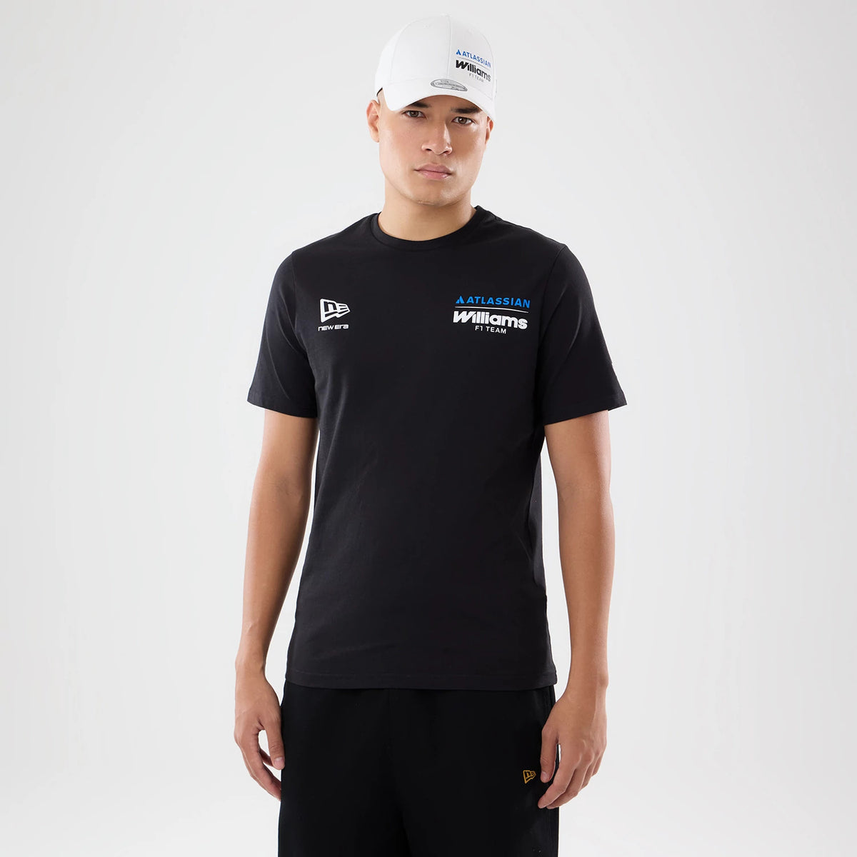 New Era Williams Carlos Sainz Spain Race Special Black T-Shirt, front view on-model displaying the New Era logo on the right chest, the Williams F1 Team logo embroidered on the left chest, and a matching cap with Atlassian branding.