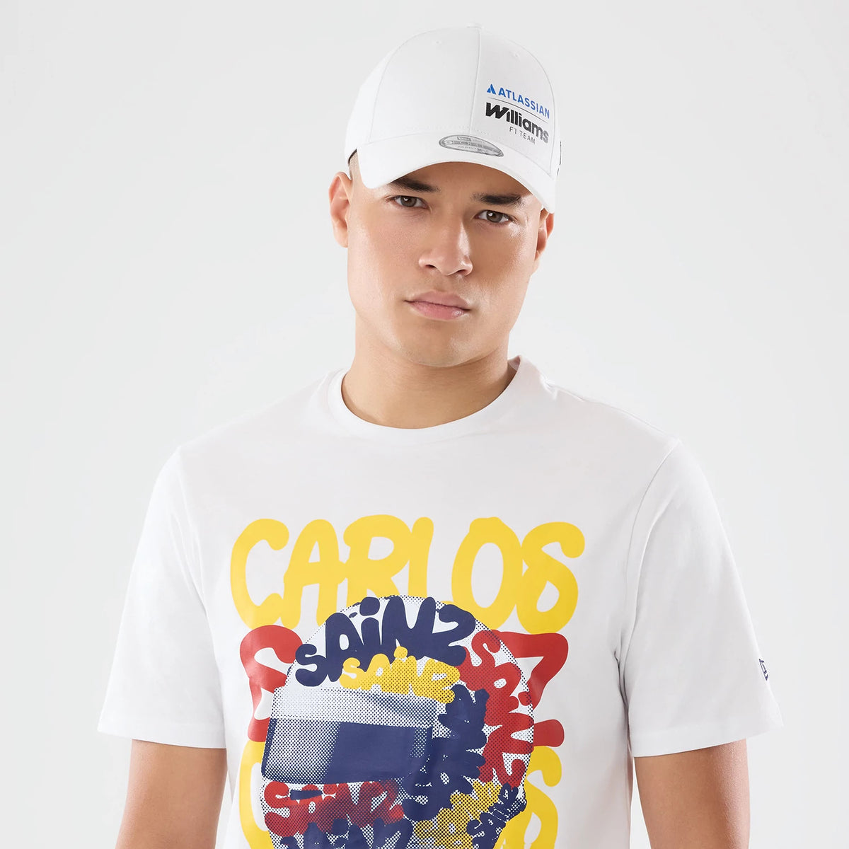 New Era Williams Carlos Sainz Spain Race Special White T-Shirt, front view on a model featuring yellow CARLOS lettering above a dynamic, abstract pattern with overlapping SAINZ inscriptions in red, yellow, and navy.
