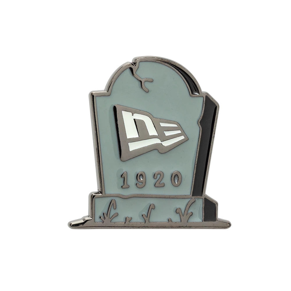 New Era Halloween Grave Grey Pin Badge, front view showing a tombstone-shaped design with a prominent debossed New Era flag logo and the year 1920 beneath, featuring branch and grass details at the base.