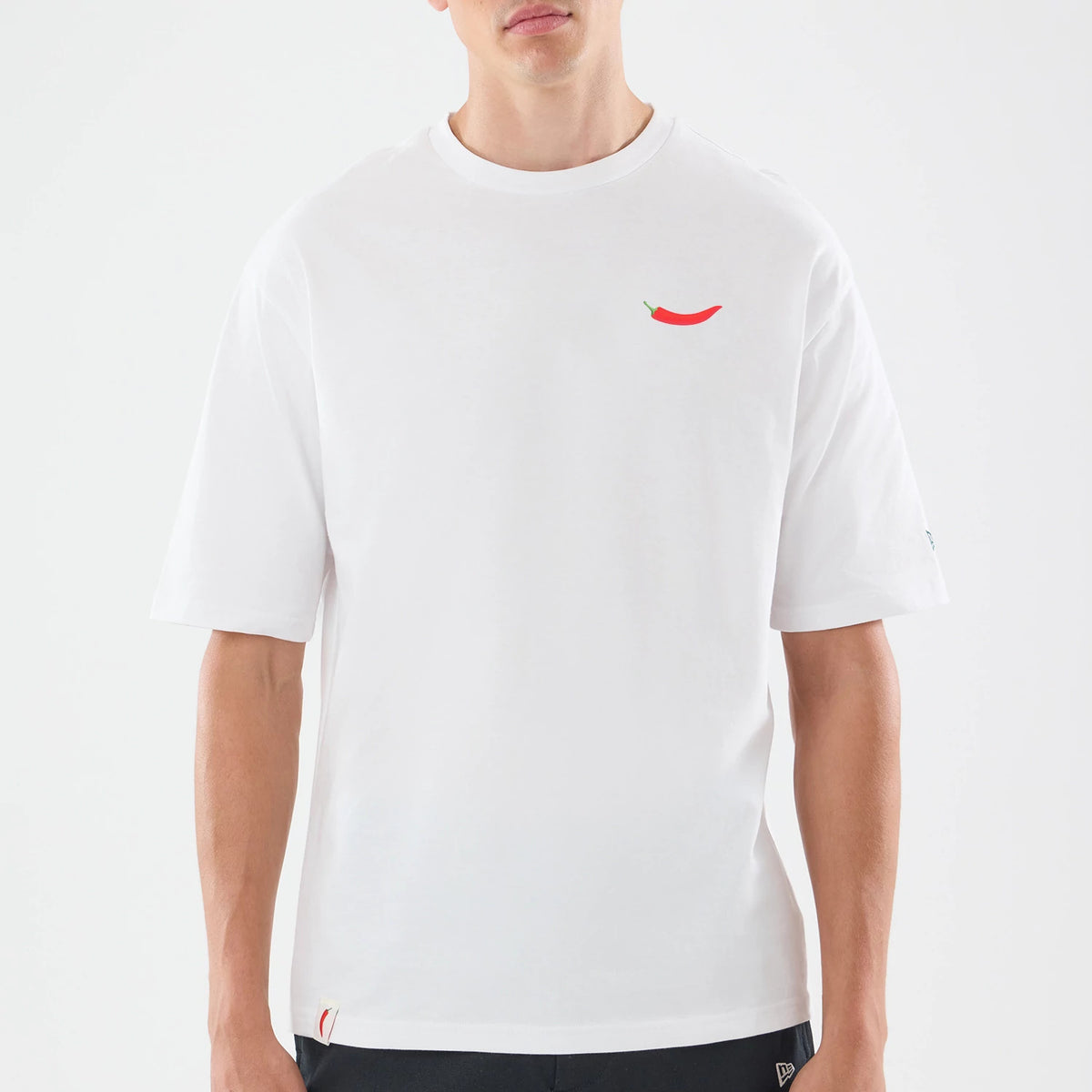 New Era Carlos Sainz Team Fifty5 White Oversized T-Shirt, front view showing a small red chilli graphic on the left chest, short sleeves, and a relaxed fit, with a New Era logo printed on the left sleeve near the hem.