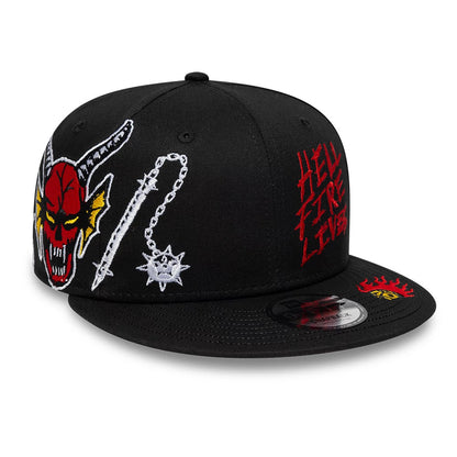 Netflix Stranger Things Hellfire Lives Black New Era 9FIFTY Snapback Adjustable Cap, three-quarter view showing the vivid red and yellow demonic face with horn embroidery on the black front panels, red Hellfire Lives text on the side.