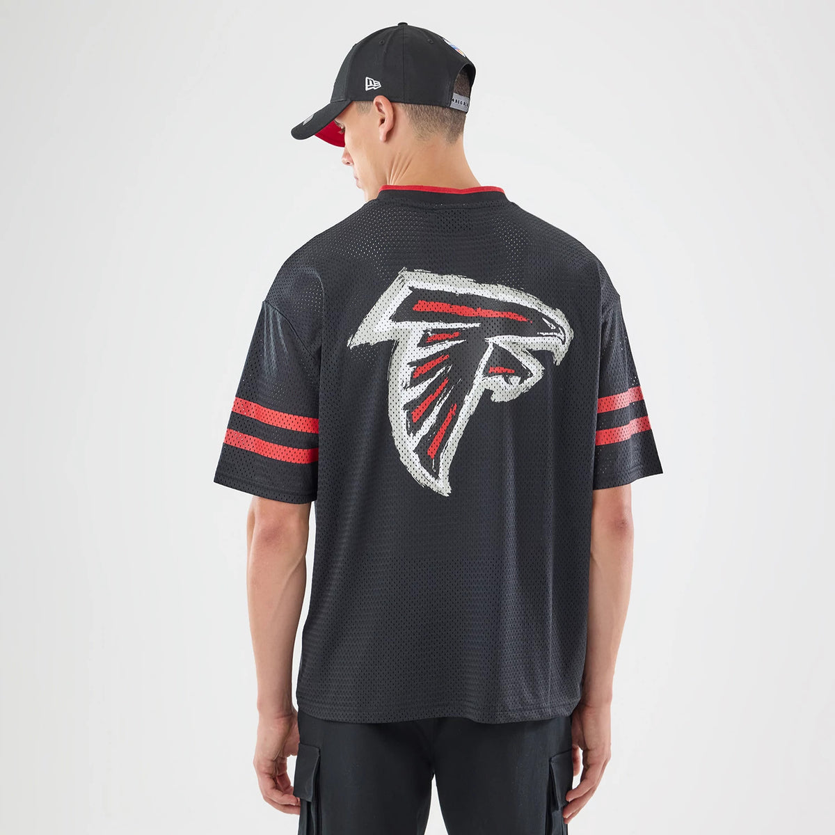 New Era Atlanta Falcons NFL International Games 2026 Graphic Black Mesh Jersey, back view on a model with a cap, showing a large Falcons logo centred on the back, red collar detail, and red stripes on the sleeves.