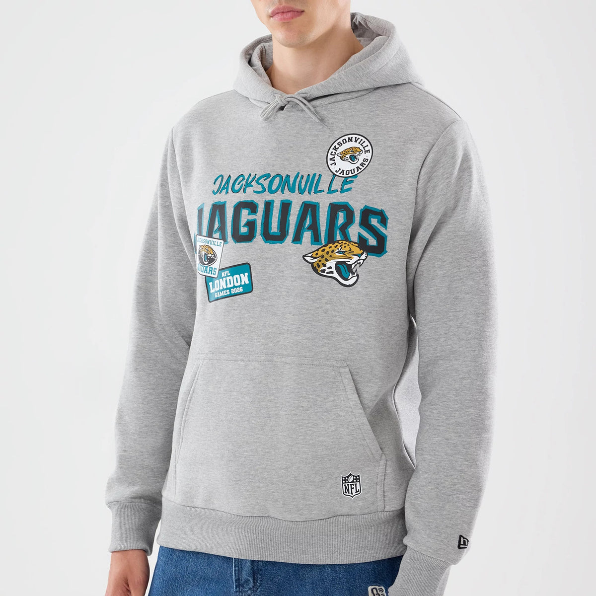 New Era Jacksonville Jaguars NFL Patch Grey Pullover Hoodie, front view on a model, featuring Jacksonville lettering in blue across the chest, a large jaguar logo below, multiple team and event patches on the front.