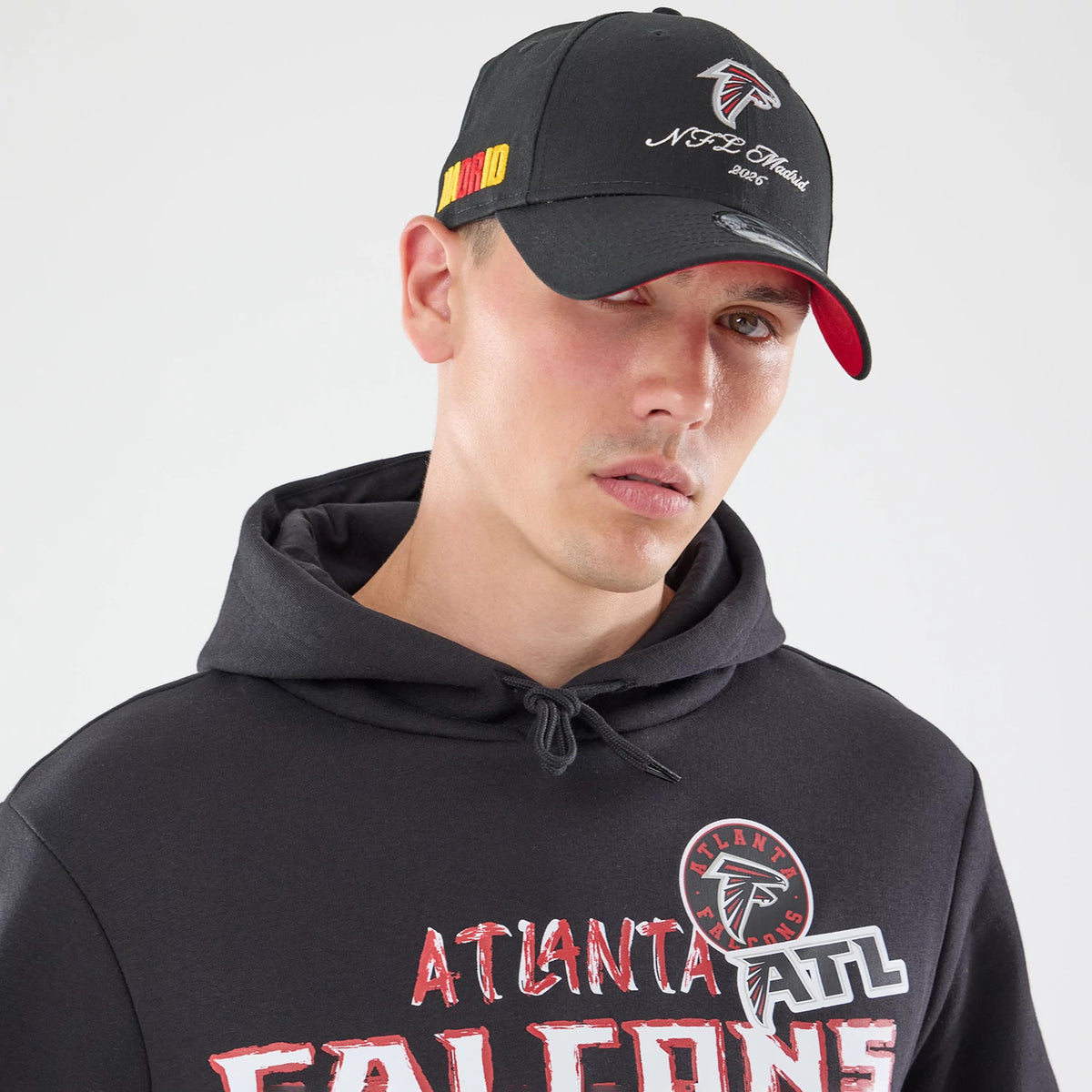 New Era Atlanta Falcons NFL Patch Black Pullover Hoodie, front view on-model highlighting the printed Atlanta Falcons logo and team name across the chest, with a drawstring hood and ribbed cuffs, paired with a black cap featuring an embroidered logo.