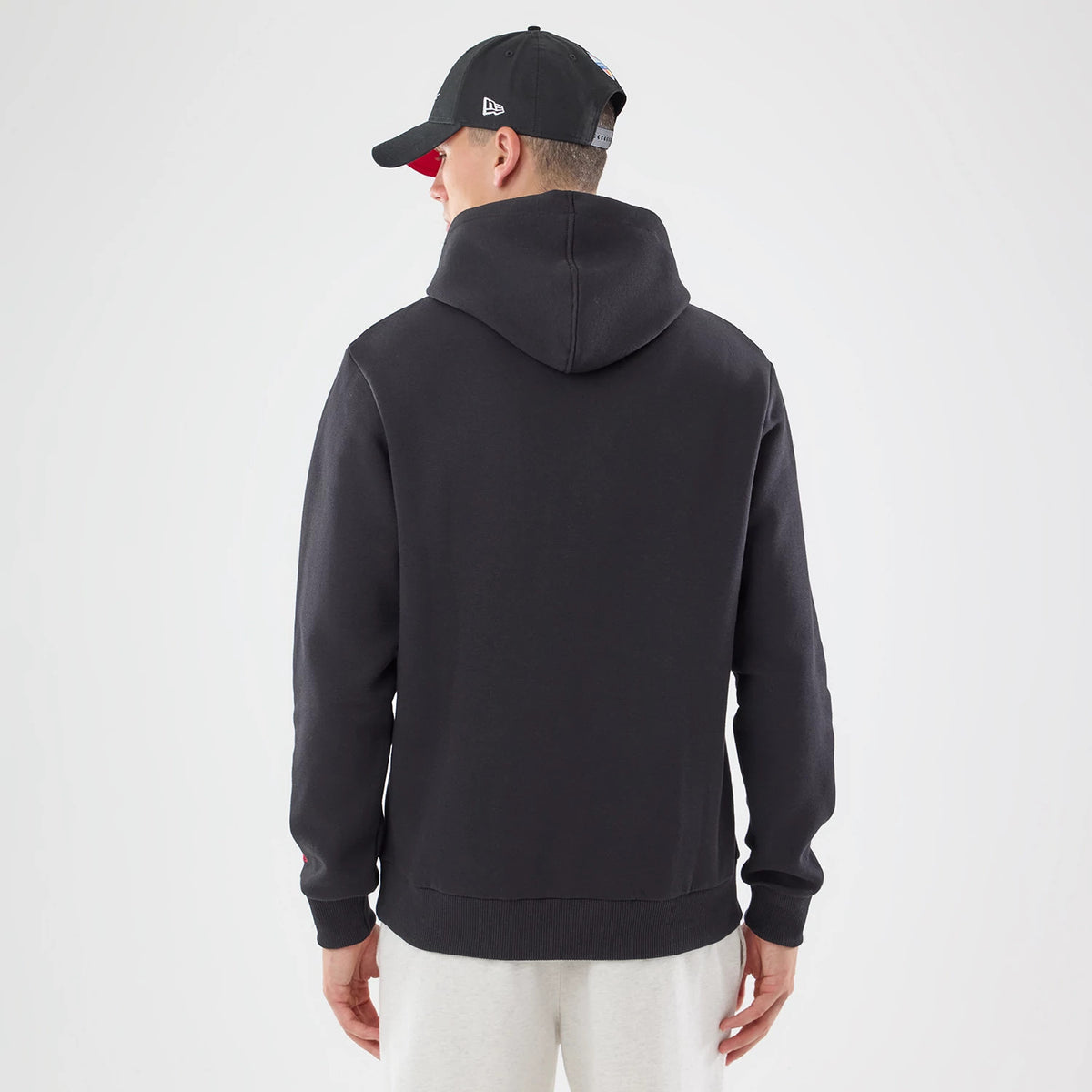 New Era Atlanta Falcons NFL Patch Black Pullover Hoodie, back view on a model also wearing a black cap, showing the plain black hoodie with a simple design, an attached hood, and ribbed cuffs and hem for a classic look.