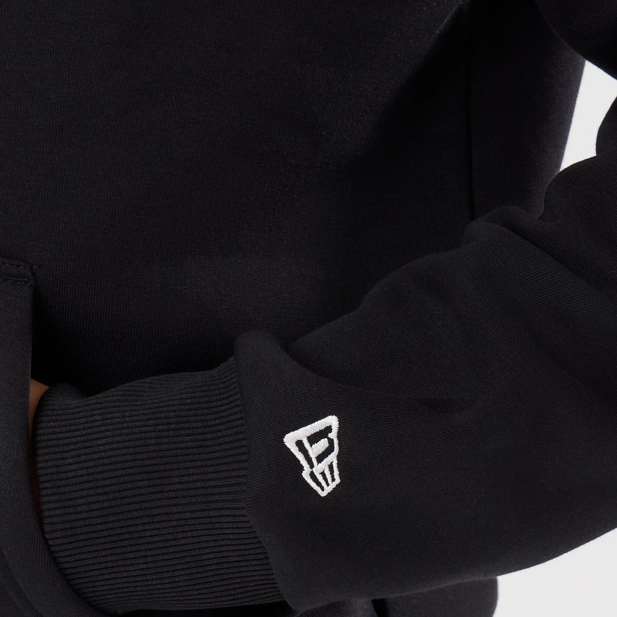 New Era Detroit Lions NFL Patch Black Pullover Hoodie, three-quarter view focused on the left sleeve featuring a white embroidered New Era logo near the ribbed cuff and a glimpse of the kangaroo pocket on the front of the hoodie.