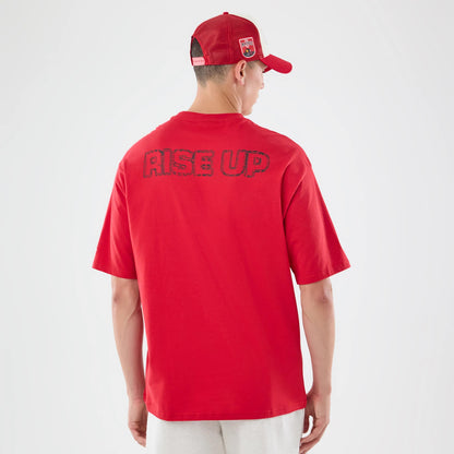 New Era Atlanta Falcons NFL Graphic Slogan Red Oversized T-Shirt, back view on a model wearing a red cap, featuring RISE UP lettering across the upper back, highlighting the red colour and loose fit of the oversized tee.