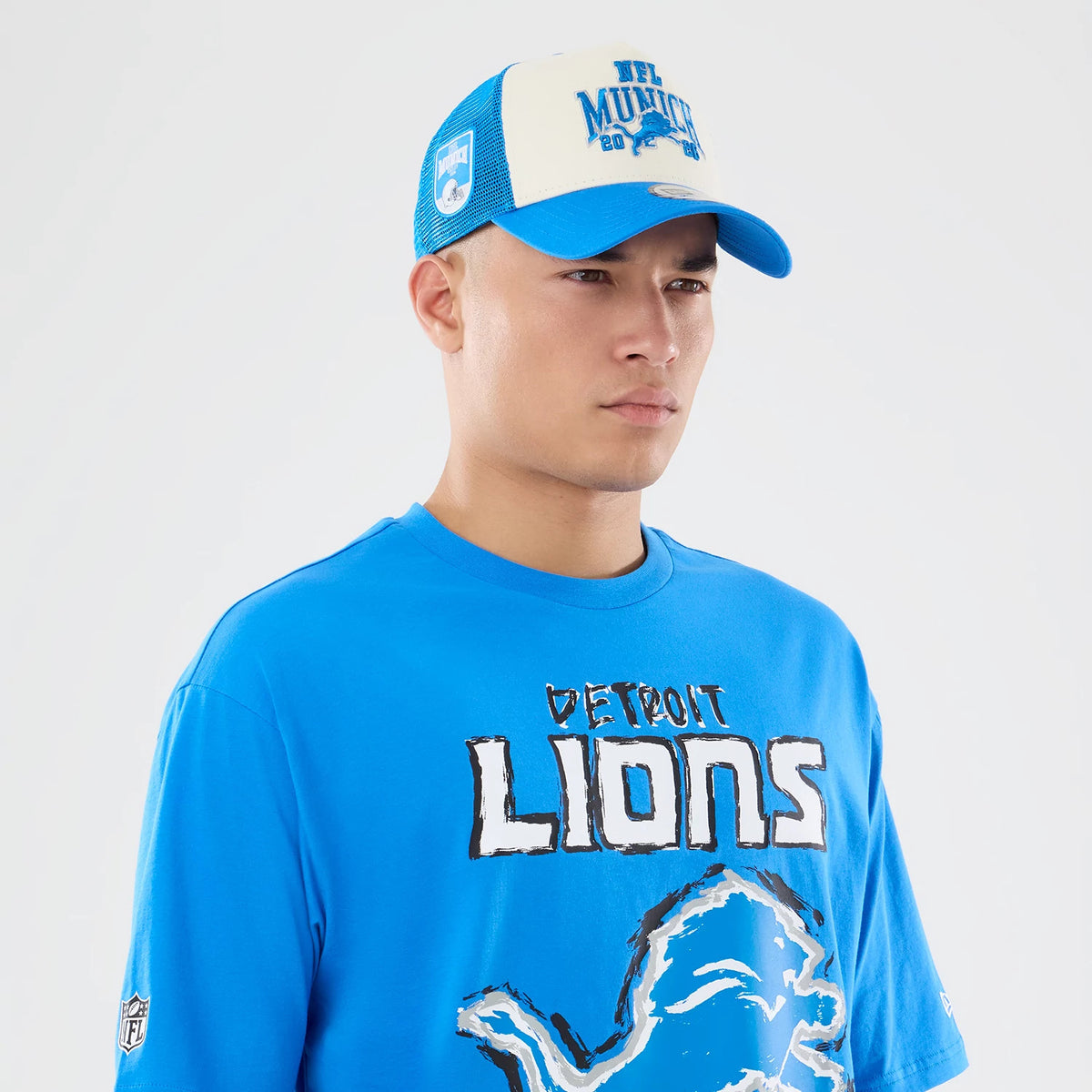 New Era Detroit Lions NFL Graphic Slogan Blue Oversized T-Shirt, front view on a model showing white DETROIT LIONS lettering across the chest with a large lion logo beneath, styled with a matching blue and white cap featuring raised graphics.