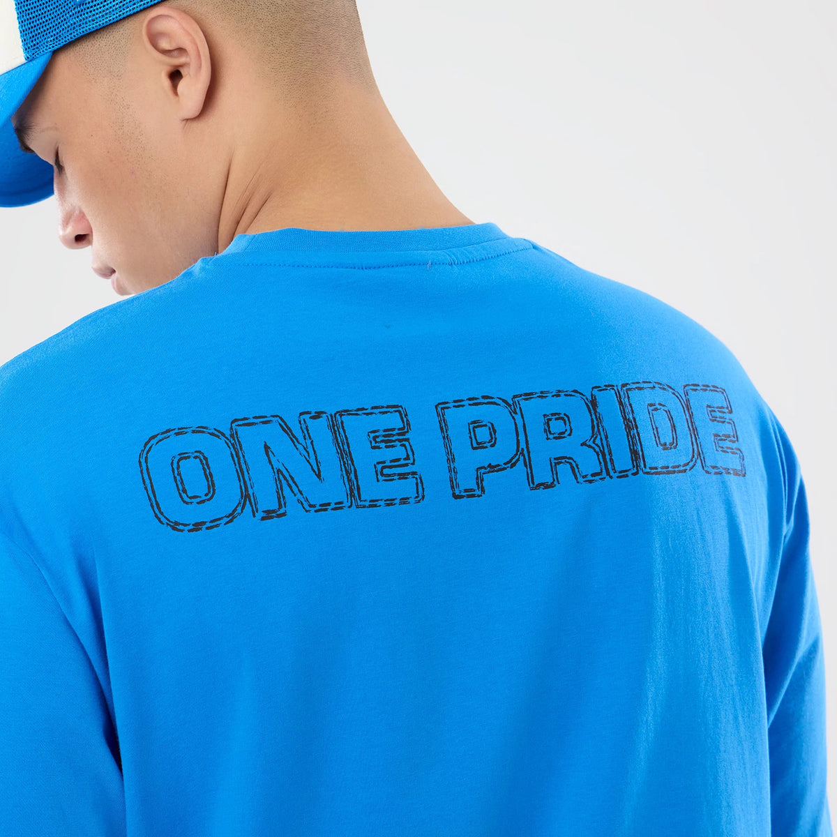 New Era Detroit Lions NFL Graphic Slogan Blue Oversized T-Shirt, back view on a model wearing a blue cap, featuring the black printed slogan ONE PRIDE across the upper back against the bright blue fabric, creating a visual effect.