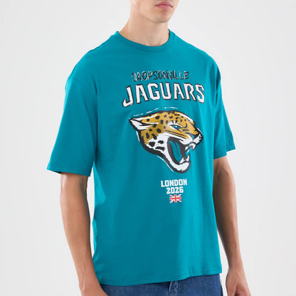New Era Jacksonville Jaguars NFL Graphic Slogan Turquoise Oversized T-Shirt, front view showing a graphic of a jaguar head beneath the Jacksonville Jaguars name, and London 2026 with a Union Jack flag near the hem, worn with blue jeans.