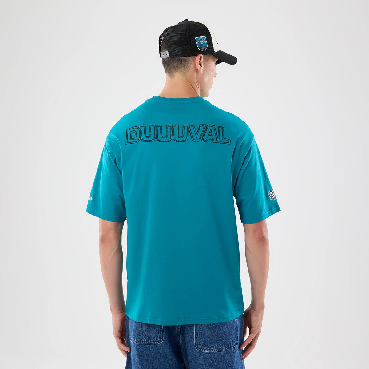 New Era Jacksonville Jaguars NFL Graphic Slogan Turquoise Oversized T-Shirt, back view on a model wearing a black cap, showcasing large embroidered DUUUVAL lettering across the upper back, with a small embroidered NFL logo on the right sleeve.