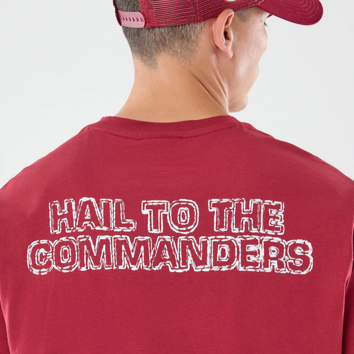 New Era Washington Commanders NFL Graphic Slogan Dark Red Oversized T-Shirt, back view on a model wearing a matching cap, displaying large white embroidered text that reads HAIL TO THE COMMANDERS across the upper back of the dark red fabric.