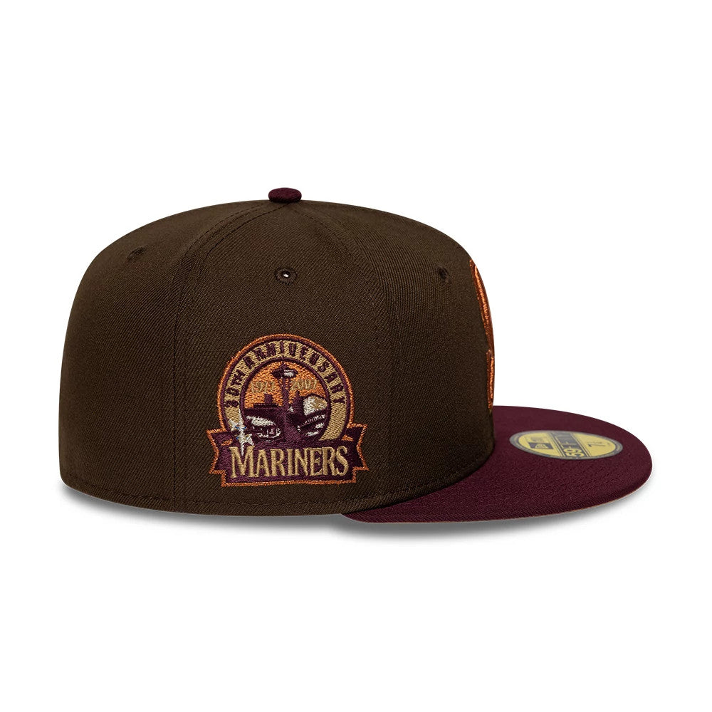Seattle Mariners MLB Cooperstown Dark Brown New Era 59FIFTY Fitted Cap, side view showing the intricate embroidered Mariners logo with orange and maroon details on the brown crown, paired with a maroon flat visor and a gold 59FIFTY size sticker.