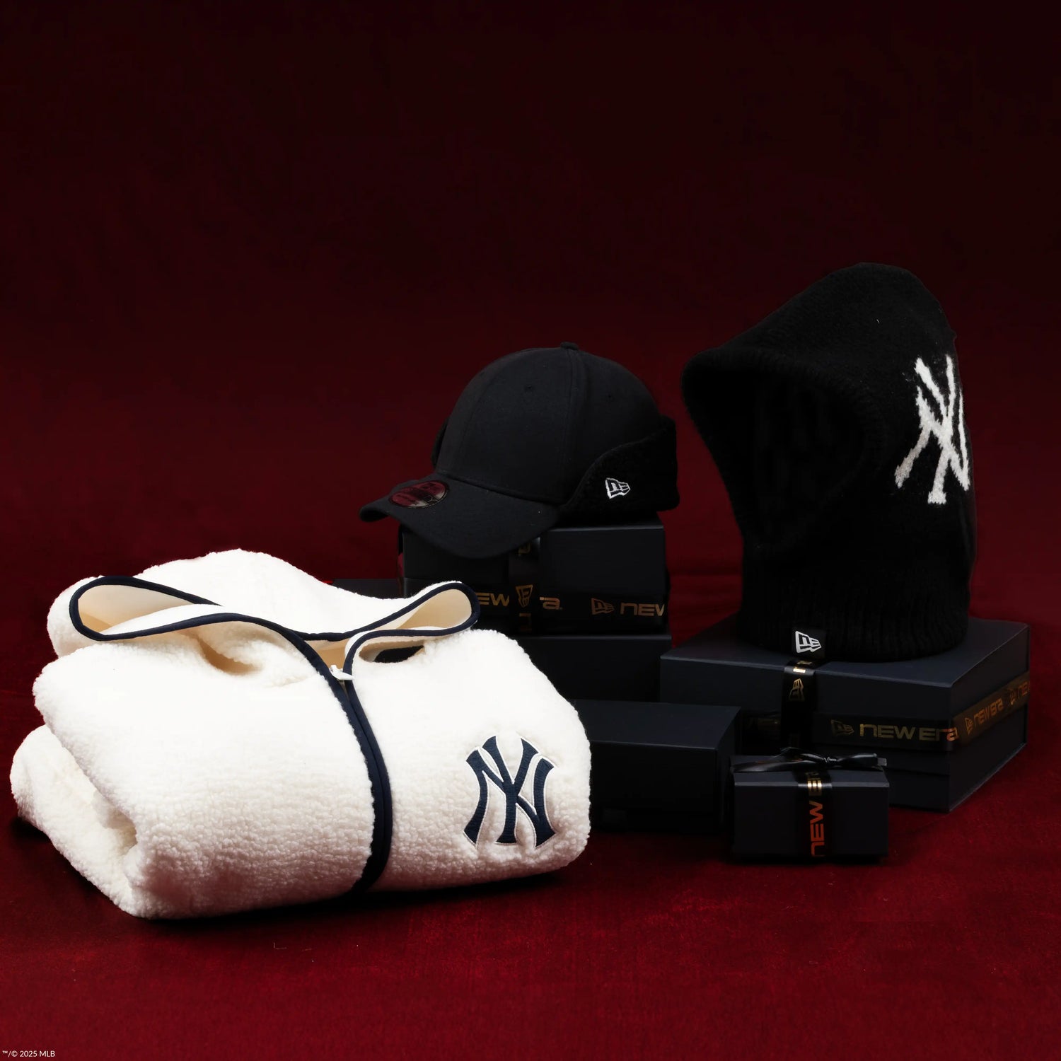 New York Yankees branded items including a towel, cap, and sweatshirt on a dark red background.