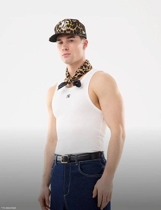 Person wearing a white tank top, leopard print cap, and scarf on a plain background