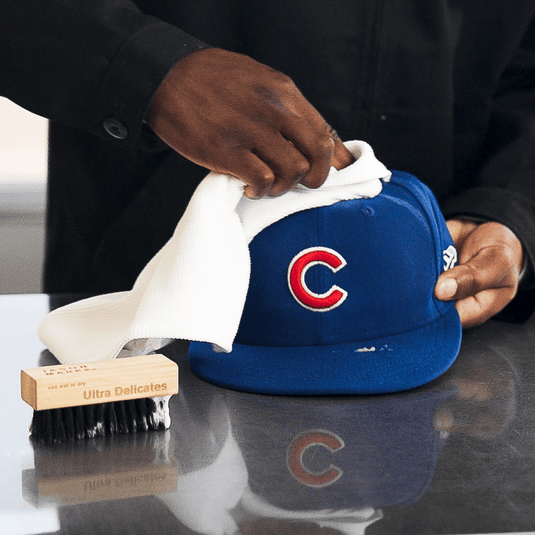 Person cleaning a blue cap with a white cloth on a reflective surface.