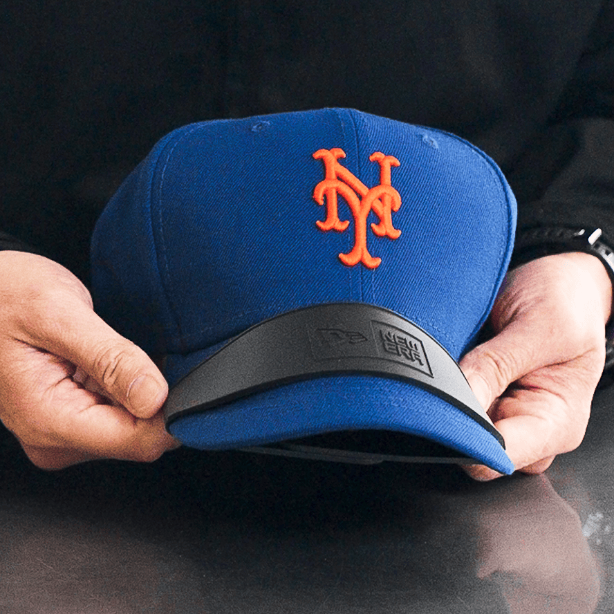 Blue baseball cap with orange logo held by a person against a black background