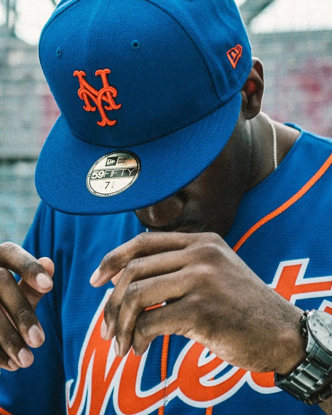 Person wearing a blue New York Mets baseball cap with orange logo and matching jersey.
