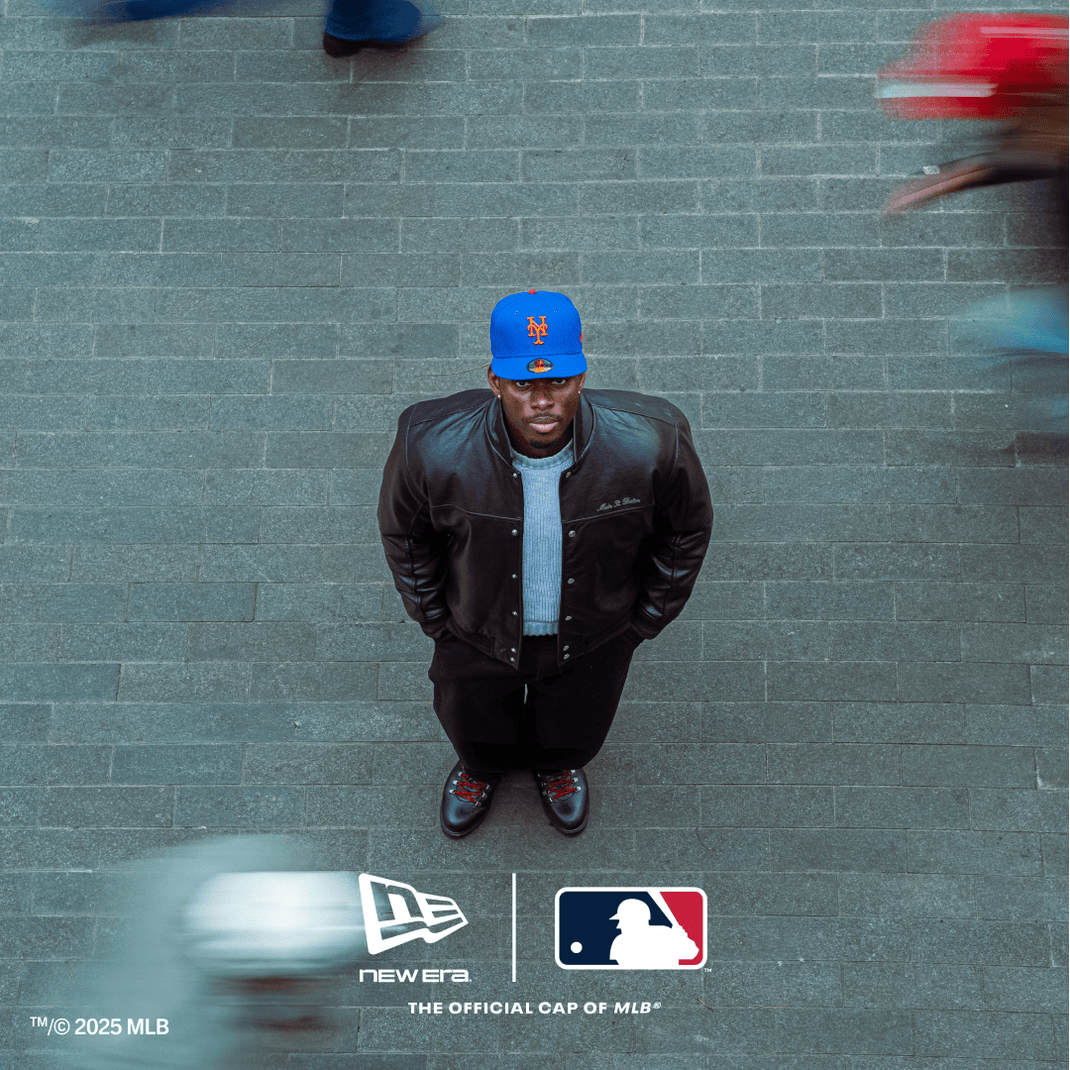 Man wearing a blue cap and leather jacket standing on a tiled floor with New Era and MLB logos.