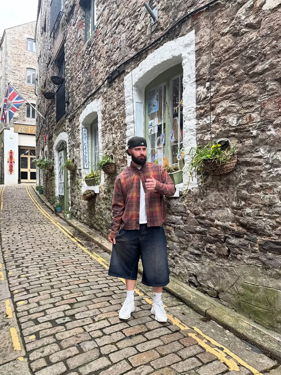 Slide 2:Man wearing a New Era Cap backwards standing on a cobbled street in an urban setting with stone buildings.