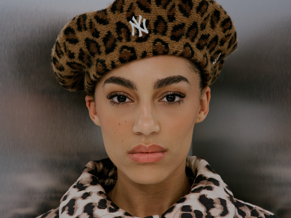Person wearing a leopard print beret with a New York Yankees logo and matching coat.
