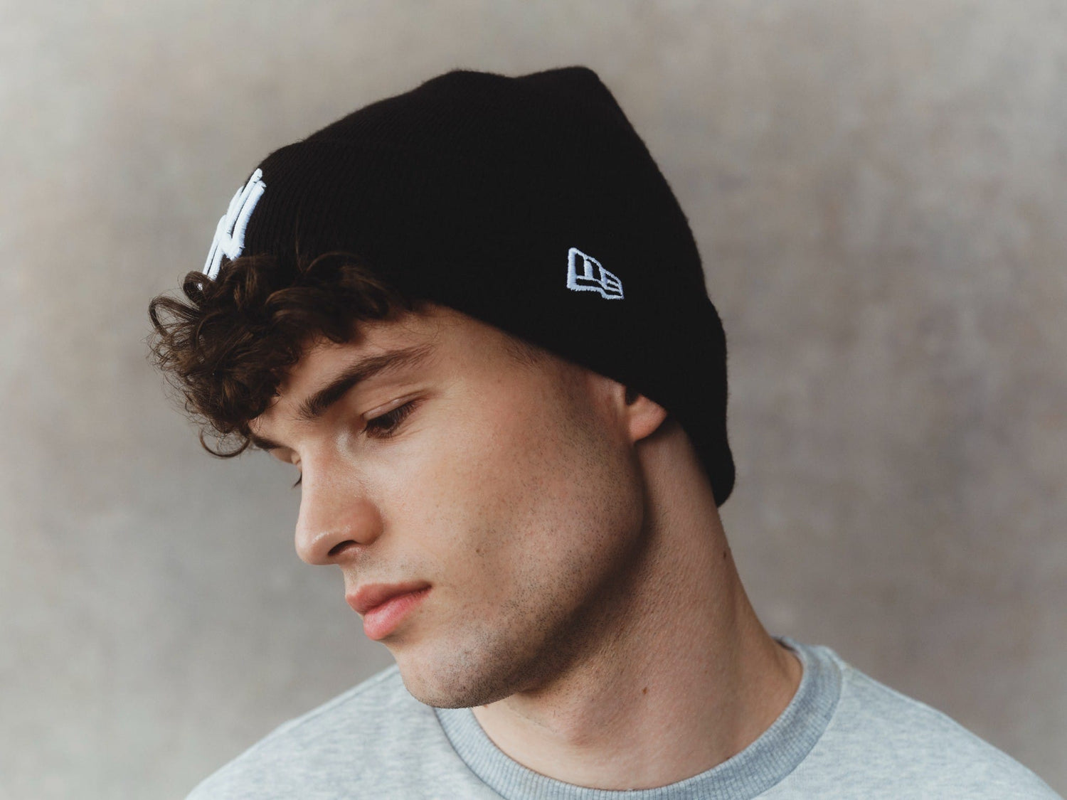 Man wearing a black new york yankees beanie with New Era logo against a neutral background