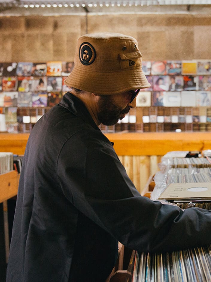 moodymann wearing a new era x moodymann beige bucket hat whilst looking through vinyls