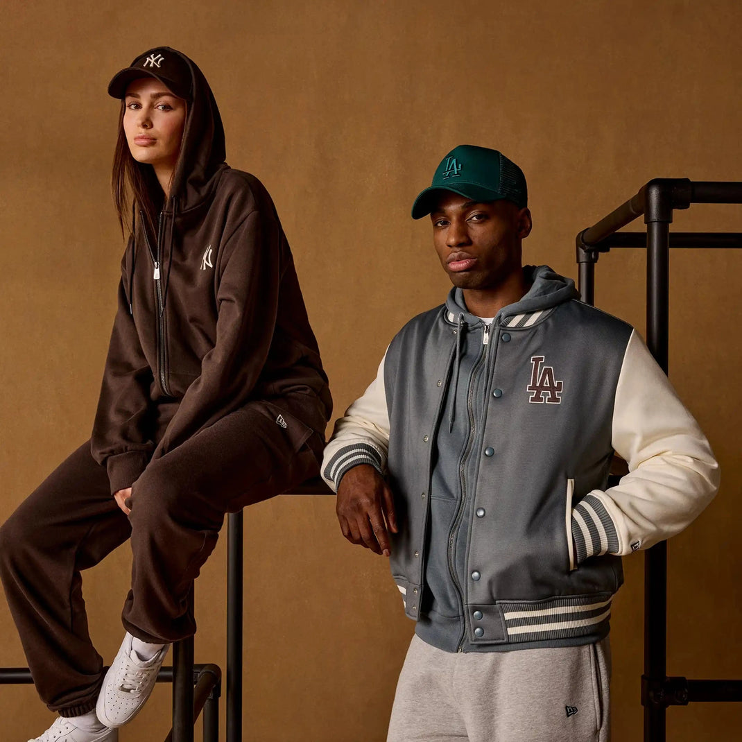 Two people wearing hoodies and caps against a brown background