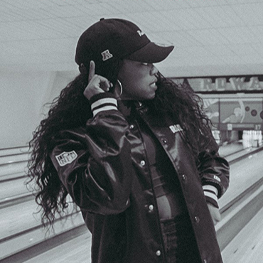Black and white image on Lady Leshurr wearing New Era Cap in a bowling alley