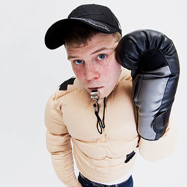 Yung Lean wearing black cap with boxing gloves on and whistle in his mouth.